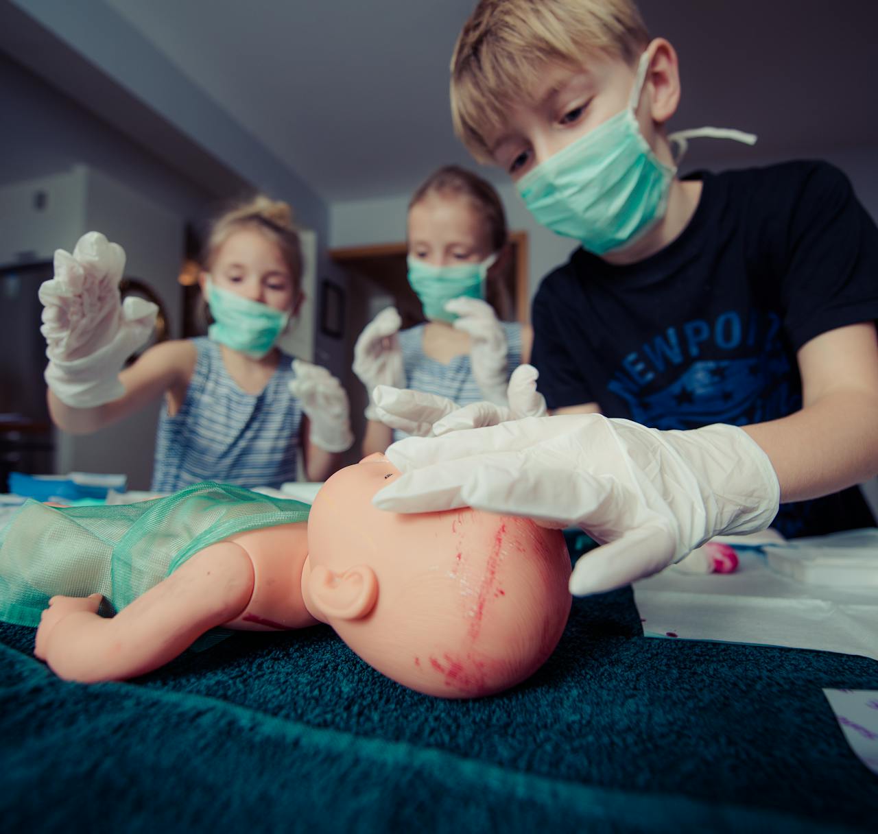 Kids role-play as surgeons indoors, using a doll to simulate first aid scenarios.